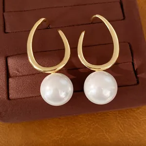 Close-up of geometric gold earrings with large white pearls on a velvet tray