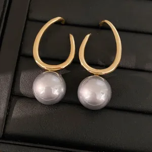 Detail showing geometric gold hoop earrings with large grey pearls on black display