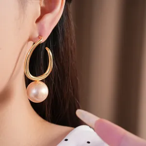 Elegant gold geometric hoop earrings with a large champagne pearl dangle on model ear