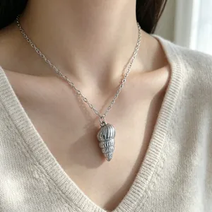 Detailed view of a stainless steel conch shell pendant necklace worn by a model.