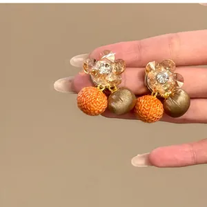 Gedetailleerde opname van zirkonia bloemenoorbellen met oranje en groene stoffen bolhangers.