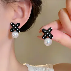 Primo piano di raffinati orecchini a forma di X a pois neri con eleganti perle bianche