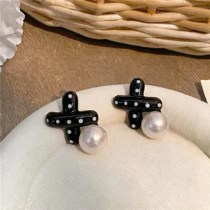 Dettaglio ravvicinato di orecchini a croce neri a pois con elegante accento di perle