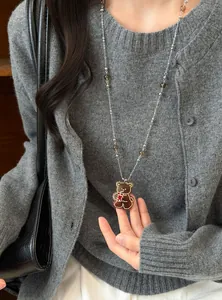 Détail du pendentif ours sur longue chaîne argentée avec perles de verre sur pull gris.