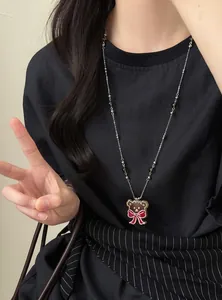 Vue détaillée d'un collier pendentif ours marron avec nœud rouge sur une longue chaîne perlée