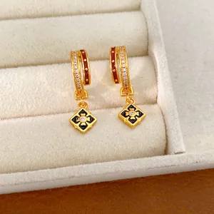 Close-up of gold earrings with red enamel and diamond-set rhombic flower pendants