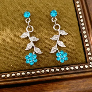 Detailansicht von silberfarbenen Ohrringen mit blauen Strassblumen und Blattdesign