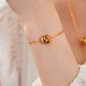 Detail view of a gold plated bracelet with burgundy enamel and zircon flower charm.