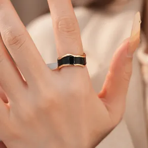 Makroaufnahme eines schwarzen Emaille-Rings mit unregelmäßigem Goldrand am Finger