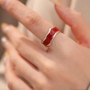 Nahaufnahme eines goldfarbenen unregelmäßigen Wellenrings mit rotem Emaille-Finish