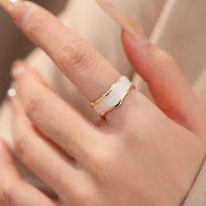 Nahaufnahme eines eleganten unregelmäßigen Wellenrings aus Gold mit weißem Emaille-Inlay