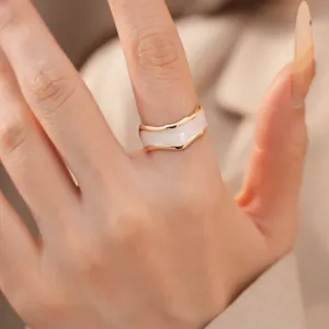 Detailansicht eines vergoldeten Rings mit unregelmäßigem weißem Emaille-Wellen-Design.