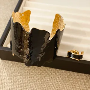 Detail eines unregelmäßigen schwarzen Emaille-Armreifs und eines passenden Goldrings