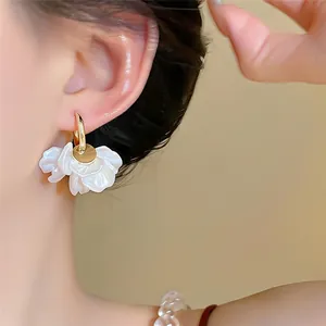 Détail macro d'élégantes boucles d'oreilles pétales blancs plaqués or 14 carats sur modèle