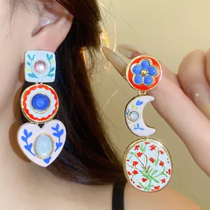 Close-up view of asymmetric resin earrings featuring colorful floral and heart patterns.