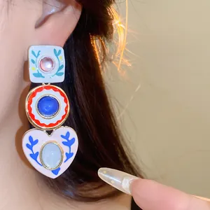 Close-up of colorful resin earrings featuring heart and geometric charms worn on ear