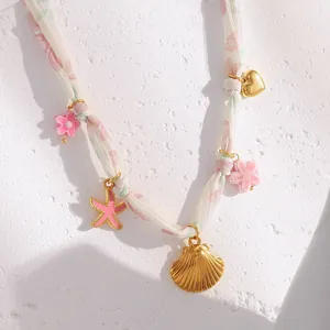 Close-up detail of golden shell and pink starfish charms on a floral ribbon necklace.