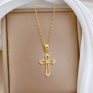 Détail du pendentif croix dorée évidée serti de cristaux sur chaîne en acier inoxydable.