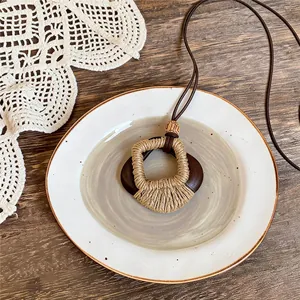 Dettaglio di collana in stile etnico con pendente in legno scuro e corda beige avvolta
