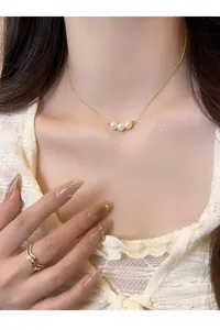 Close-up view of an elegant 18k gold plated necklace with three pearls worn by a model