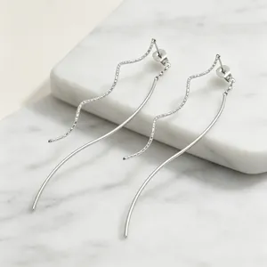 Gros plan détaillé de boucles d'oreilles vagues en acier sur une plaque de marbre blanc.