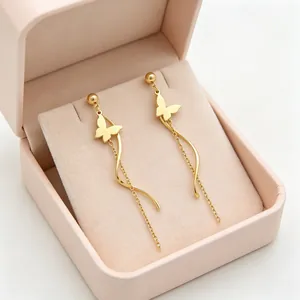 Boucles d'oreilles papillon dorées avec pompons dans une boîte rose.