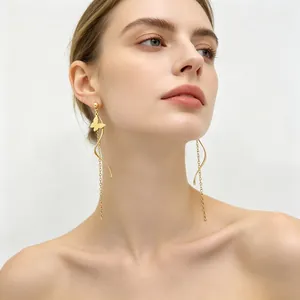 Élégantes boucles d'oreilles à pompons avec papillon doré et lignes torsadées sur modèle.