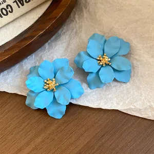 Nahaufnahme von hellblauen Blumenohrsteckern mit goldener Mitte und matter Oberfläche.