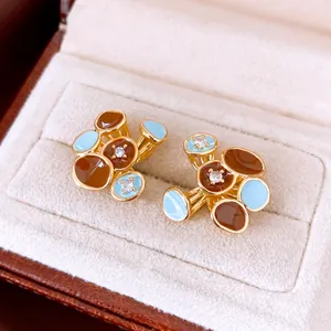 Detail van 18k vergulde bloem oorknopjes met bruin en blauw emaille voor een luxe look