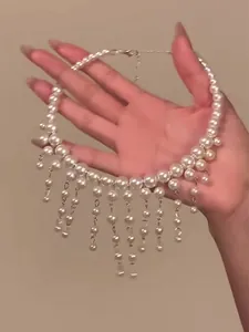 A detailed macro view of a white pearl tassel choker necklace held in a person's hand