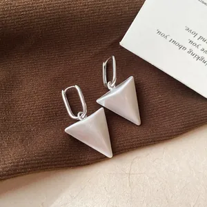 Detailopname van elegante zilverkleurige driehoekige hangoorbellen op bruine achtergrond