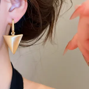 Detailopname van een minimalistische gouden driehoekige hanger oorbel bij model