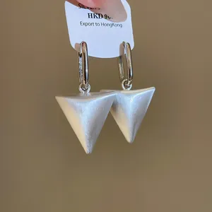 Gedetailleerde close-up van de geborstelde metalen textuur van deze zilveren driehoek oorbellen