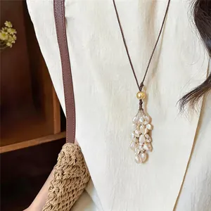 Detailaufnahme einer Vintage-Halskette mit Muschelquasten auf einem cremefarbenen Oberteil