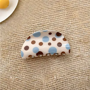 Dettaglio di una molletta per capelli in acrilico beige con pois blu e marroni