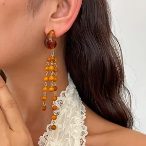 Close-up of vintage resin water drop earrings with layered wooden bead tassels on a model
