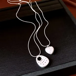 Dettaglio dei ciondoli minimalisti a cuore e ovali con motivo a pois su collana