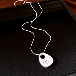 Primo piano della collana con ciondolo ovale bianco a pois neri su vassoio nero