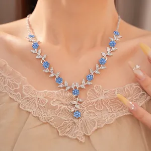 Detailopname van een elegante zilveren bloemenketting met blauwe stras en bladmotieven.