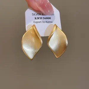 Detaillierte Makroansicht goldener, gebürsteter Blatt-Ohrstecker auf weißer Displaykarte