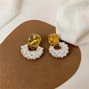 Détail de boucles d'oreilles élégantes en perles avec un carré doré et perles blanches