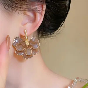 A close-up detail shot of an elegant brown enamel flower drop earring worn on a model