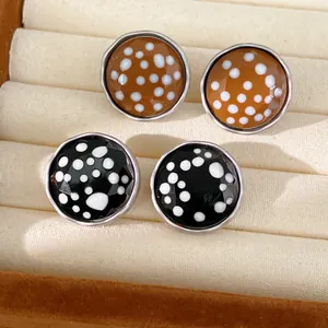 Close-up of two pairs of round polka dot stud earrings in brown and black