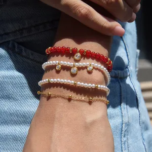 Close-up detail of layered stainless steel bracelets featuring red agate and pearls
