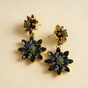 Detailopname van vintage gouden oorbellen met dubbellaagse blauwe en groene kristallen bloemen.