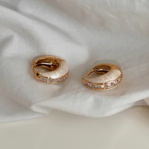 Nahaufnahme französischer Vintage-Goldohrringe mit weißem Emaille und klarem Zirkonia.