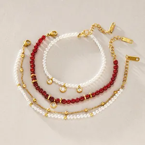 Detail view of stacked gold-tone stainless steel bracelets with red beads and pearls.