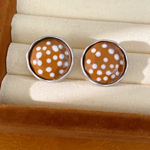 Macro view of ochre polka dot round stud earrings with a faceted glass finish and silver rim