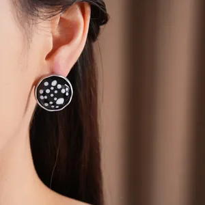 Close-up of minimalist round black glass stud earrings with white polka dots on model ear