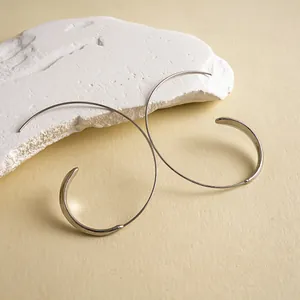 Detailed view of silver minimalist C-shaped geometric hoop earrings on textured stone background
